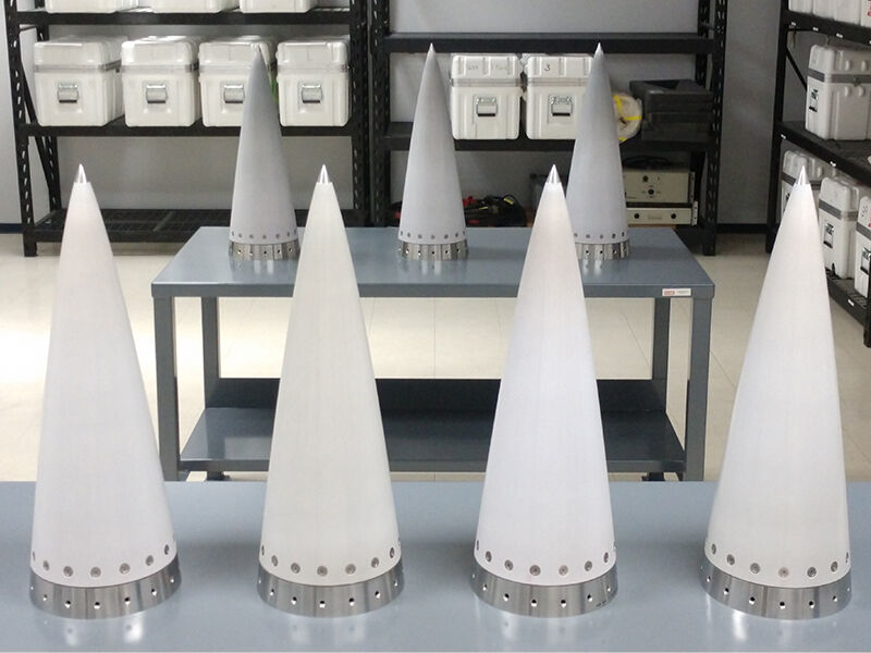 Room with two tables and shelving units. There are several white, cone-shaped CMC radomes lined up on both tables.